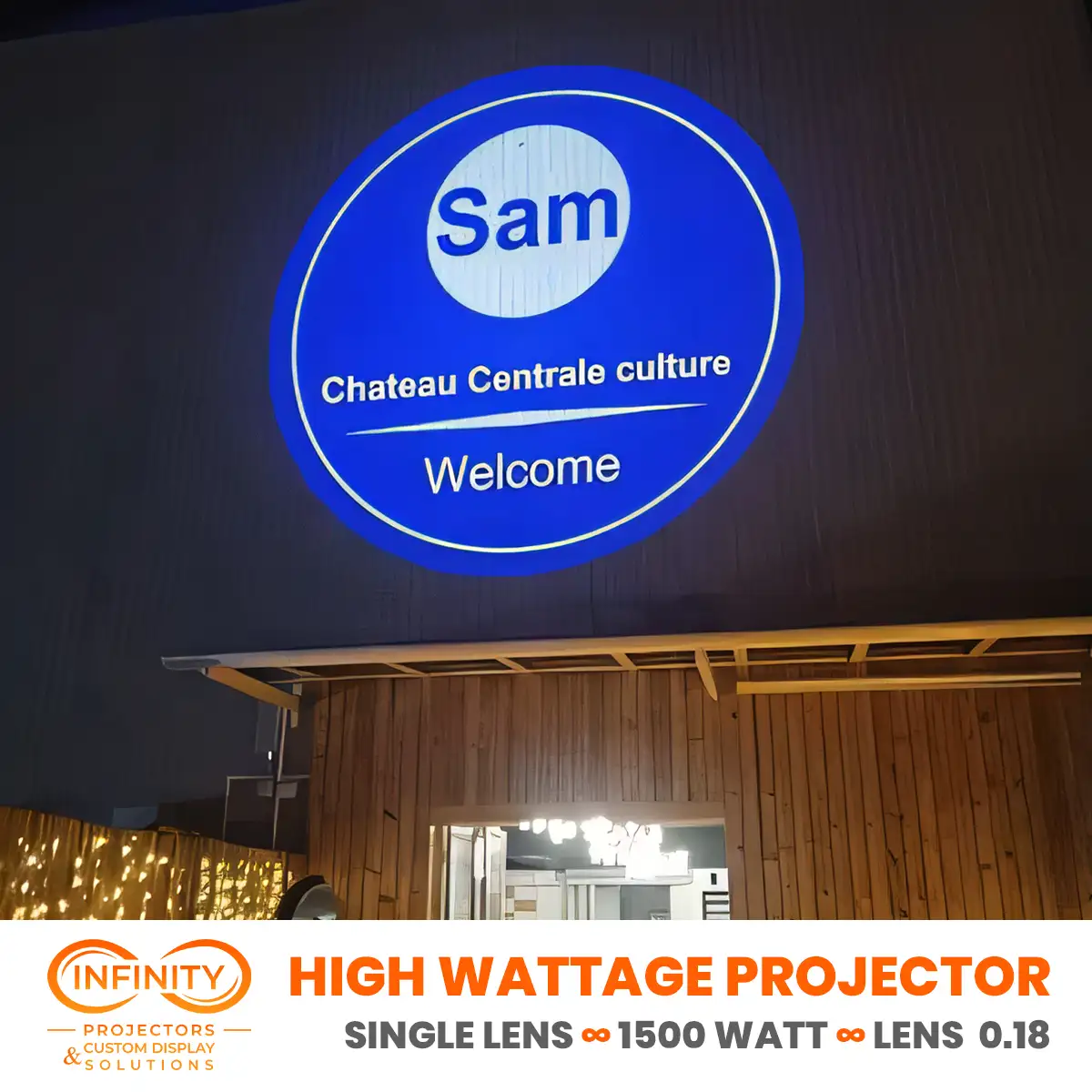 Blue circular welcome sign for a cultural venue beamed above a wooden storefront at night with an outdoor logo projector — Infinity Projectors