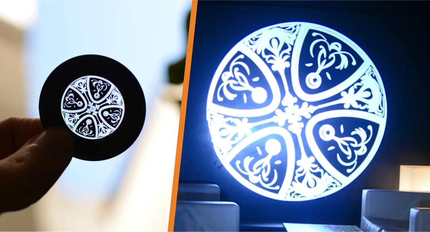 Ornate white filigree gobo pattern projected large on an indoor wall beside the small glass disc