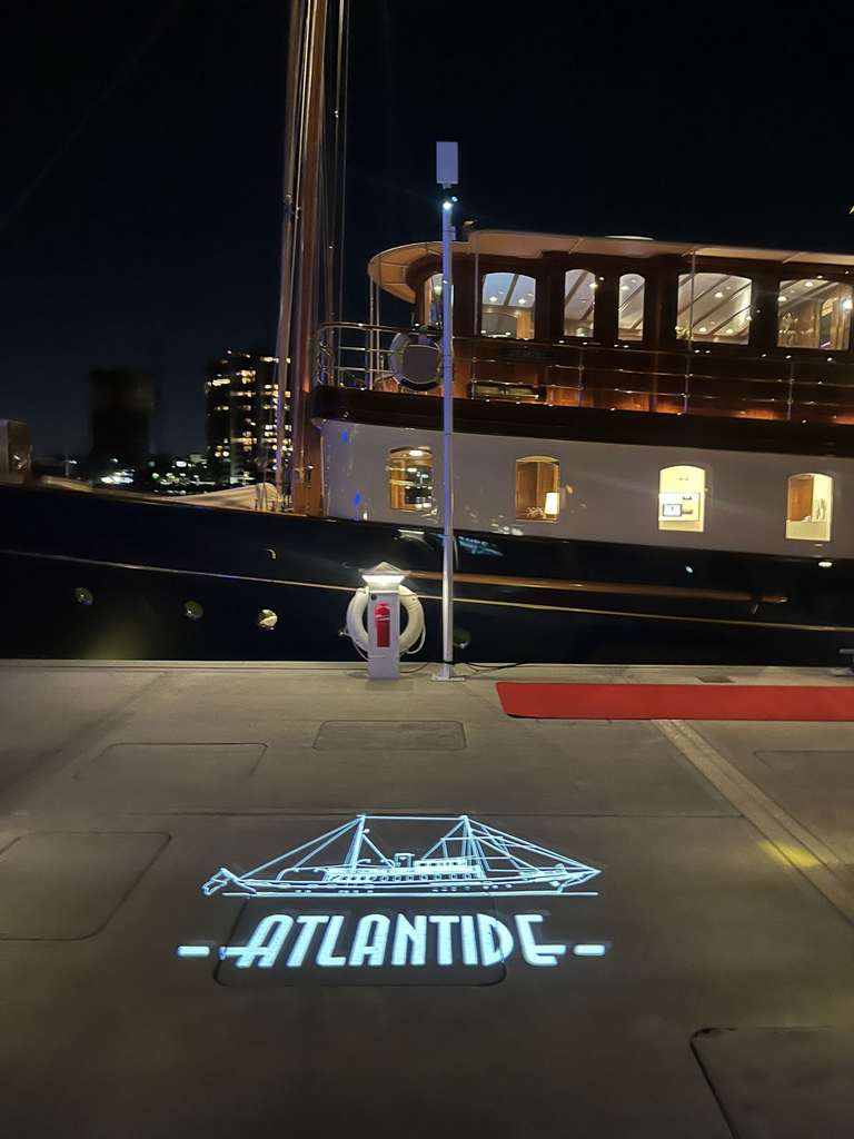 Ship-outline gobo with the vessel's name projected on the dock beside a classic yacht at night — Infinity Projectors