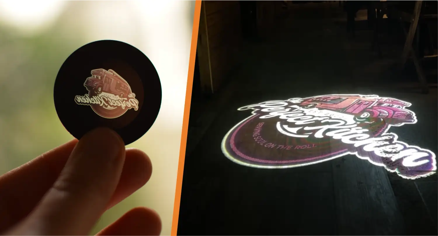 Glass gobo of a food truck logo in hand beside the glowing logo projected on a dark wood floor