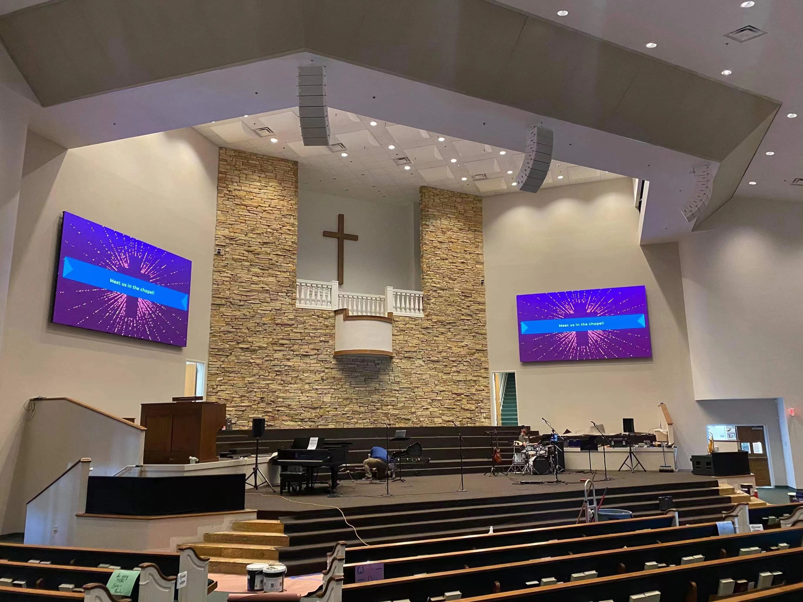 Twin LED video walls flanking a stone wall and wooden cross in a church sanctuary during setup — Infinity Projectors
