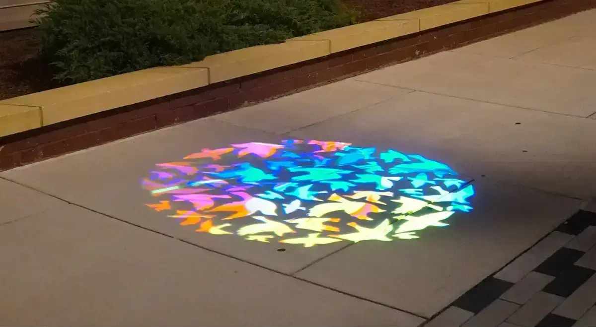Multicolored bird gobo projected in a circle on the sidewalk outside a bar entrance at night
