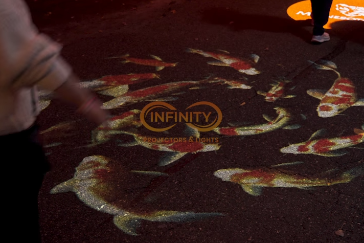 Video: koi fish gobos swim across dark pavement at night as pedestrians walk through the projection