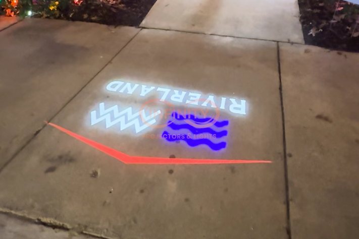 Real photo of Riverland logo projected on sidewalk at night