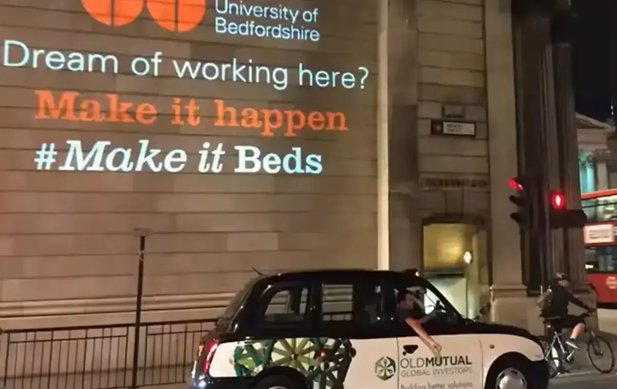 Recruitment message and leaf logo beamed onto a stone building facade at night from an outdoor logo projector