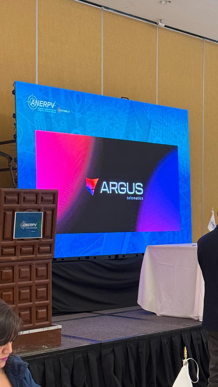 Conference stage LED screen showing a tech company's logo beside a carved wooden lectern — Infinity Projectors