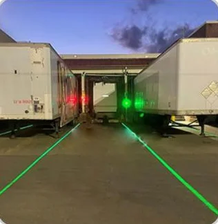Green laser lines projected between parked trailers at a truck loading dock at dusk — Infinity Projectors