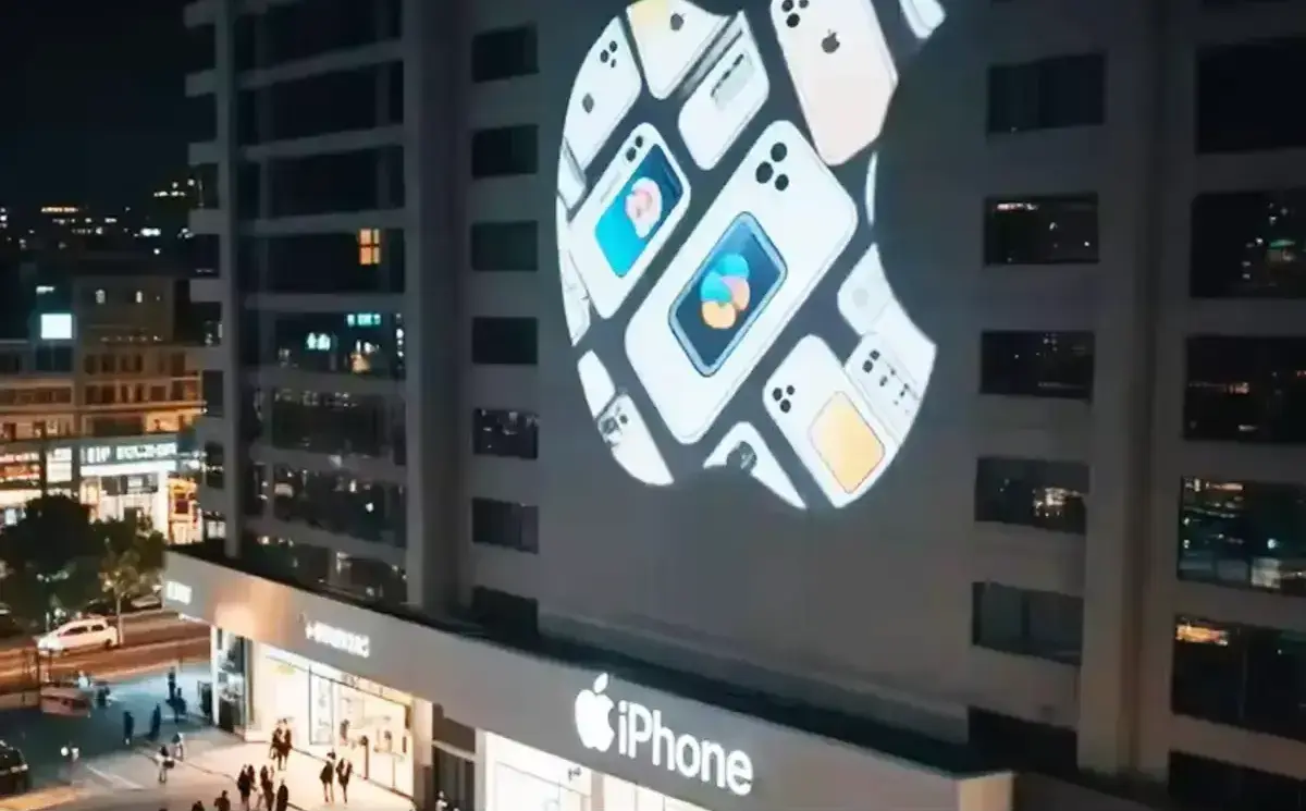 A tech giant's fruit logo formed from phone images projected on a high-rise above its brightly lit storefront — Infinity Projectors